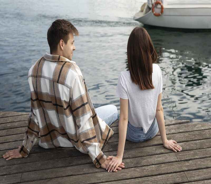 Couple sitting on a dock holding hands, enjoying a peaceful moment by the water.