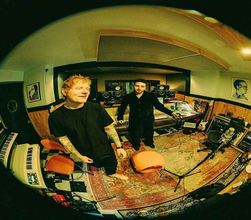 Ed Sheeran in a music studio with a collaborator, surrounded by recording equipment.